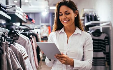 A woman in a clothing store looking at a tablet and smiling.